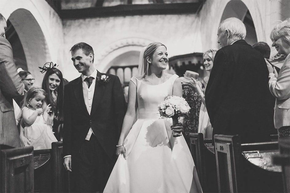 Bride smiles at her grandfather as she walks down the aisle at a church.