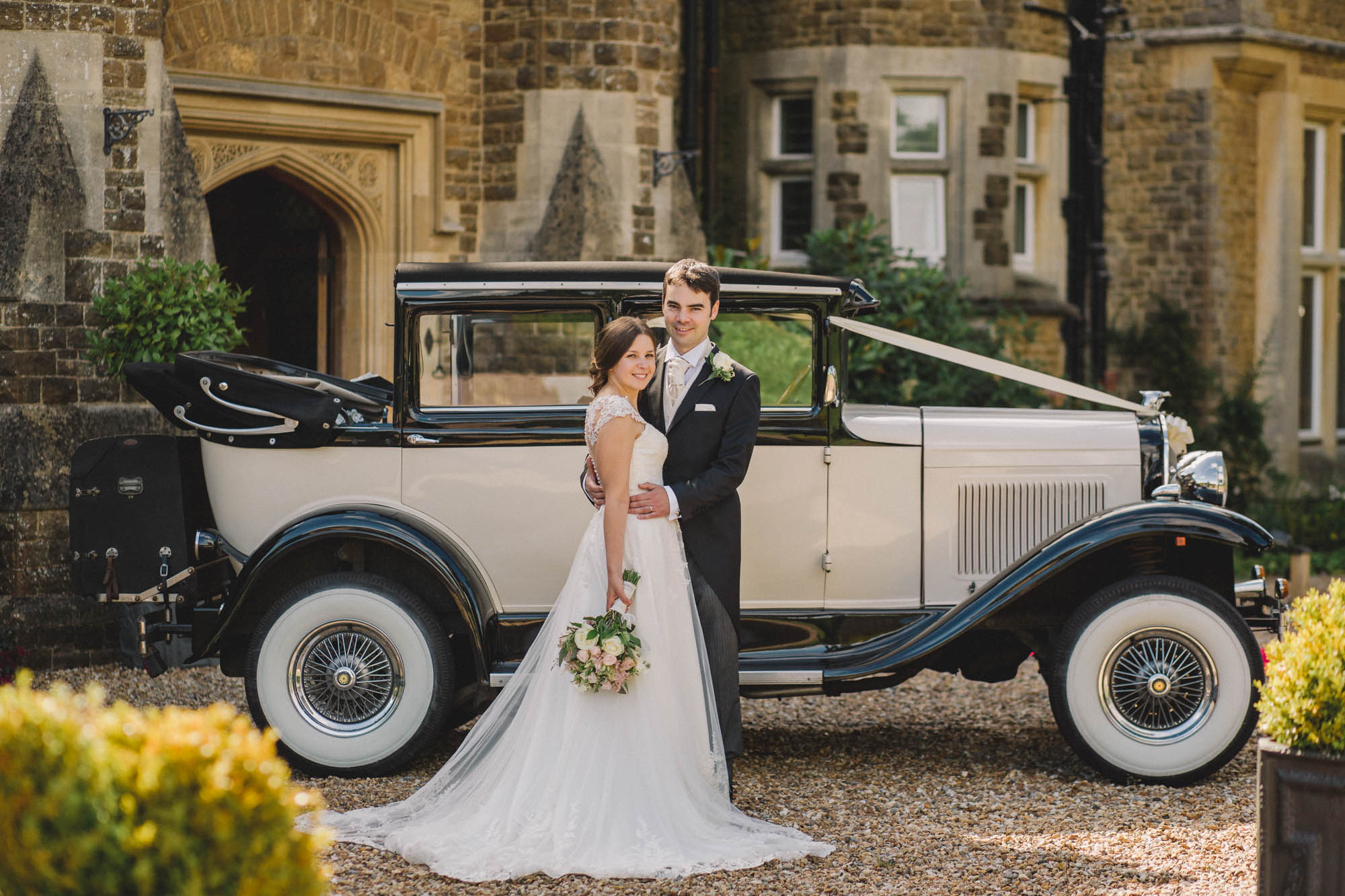 Bride and groom hug closely in front of their Rolls Royce on their wedding day at Hartsfield Manor.