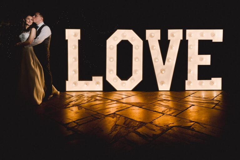 Bride and groom hug closely in front of a Love sign on their wedding day at Northbrook Park.