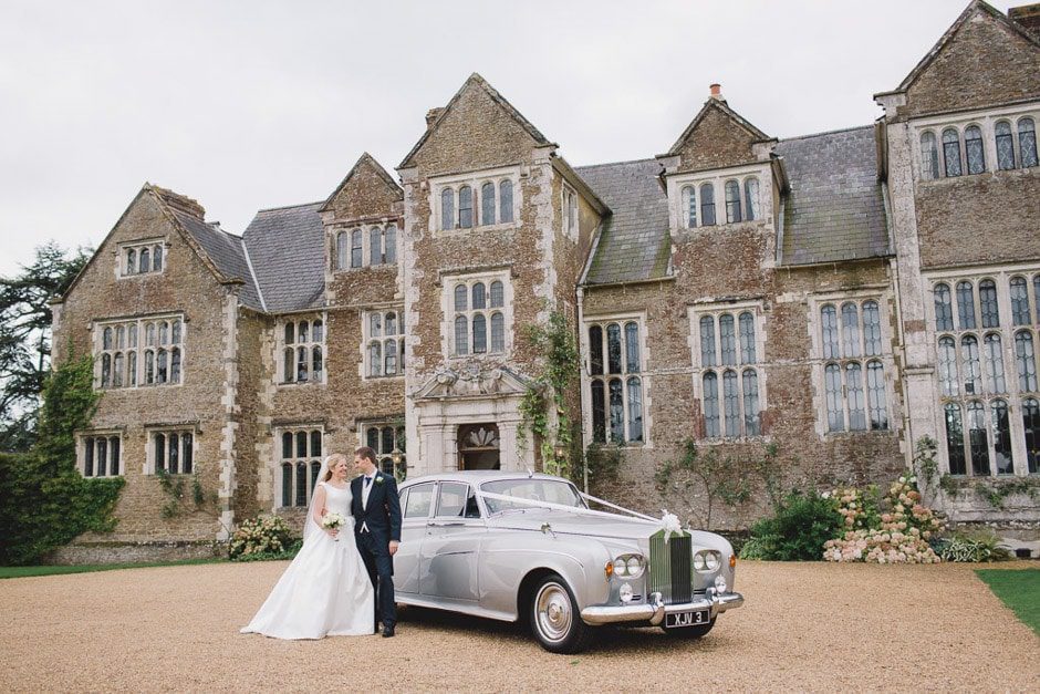 Bride and groom hug closely on their wedding day with their Rolls Royce car at Loseley Park in Surrey.