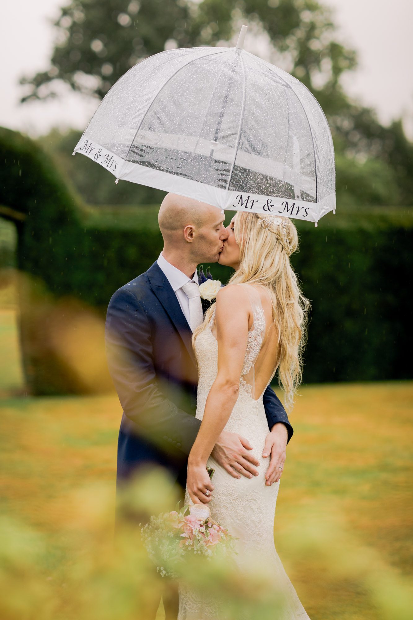 Bride and groom kiss on their wedding day under an umbrella at Barnett Hill in Surrey.