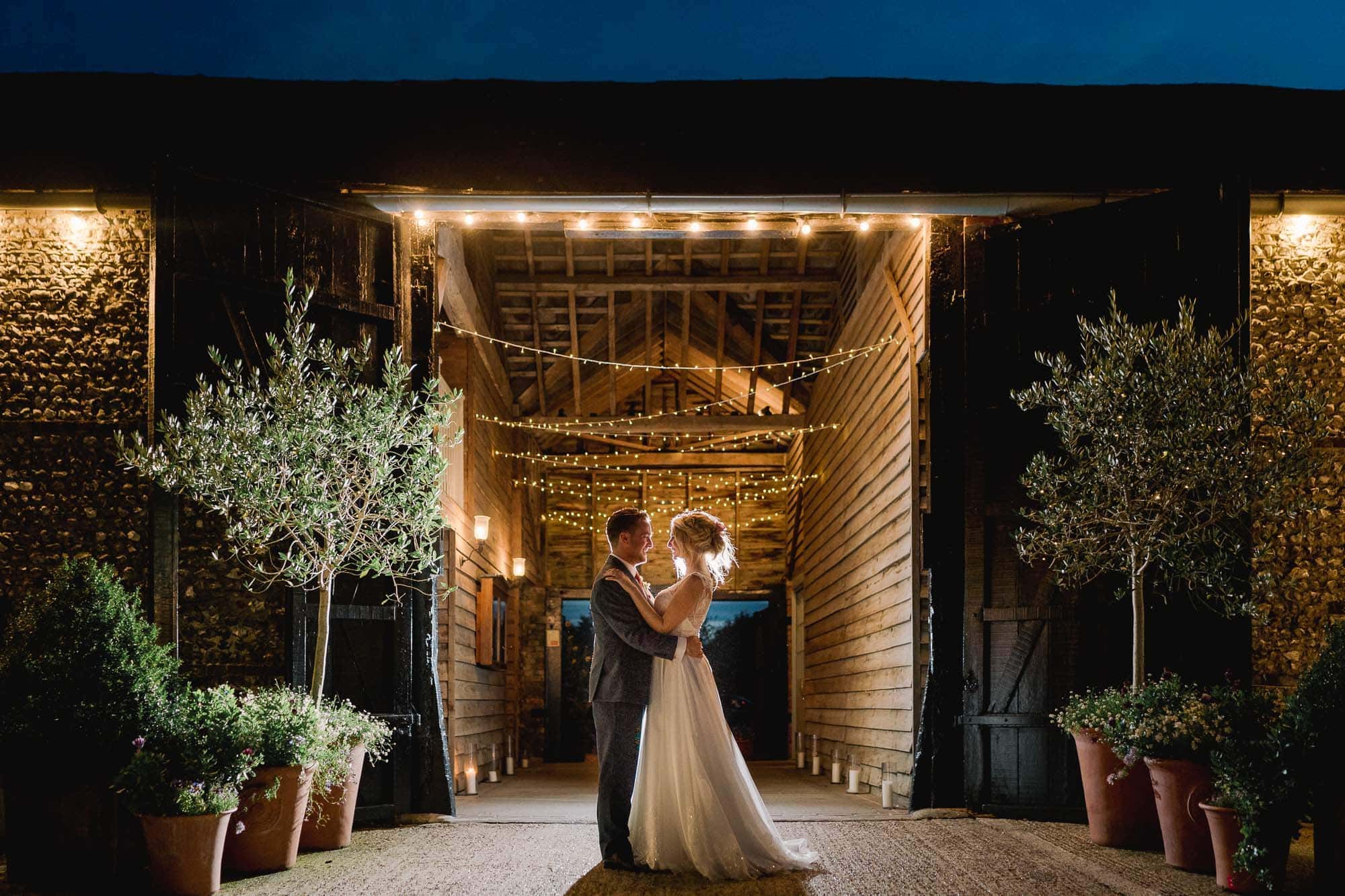 Upwaltham Barns Wedding Venue in Sussex with a bride and groom hugging in the foreground.