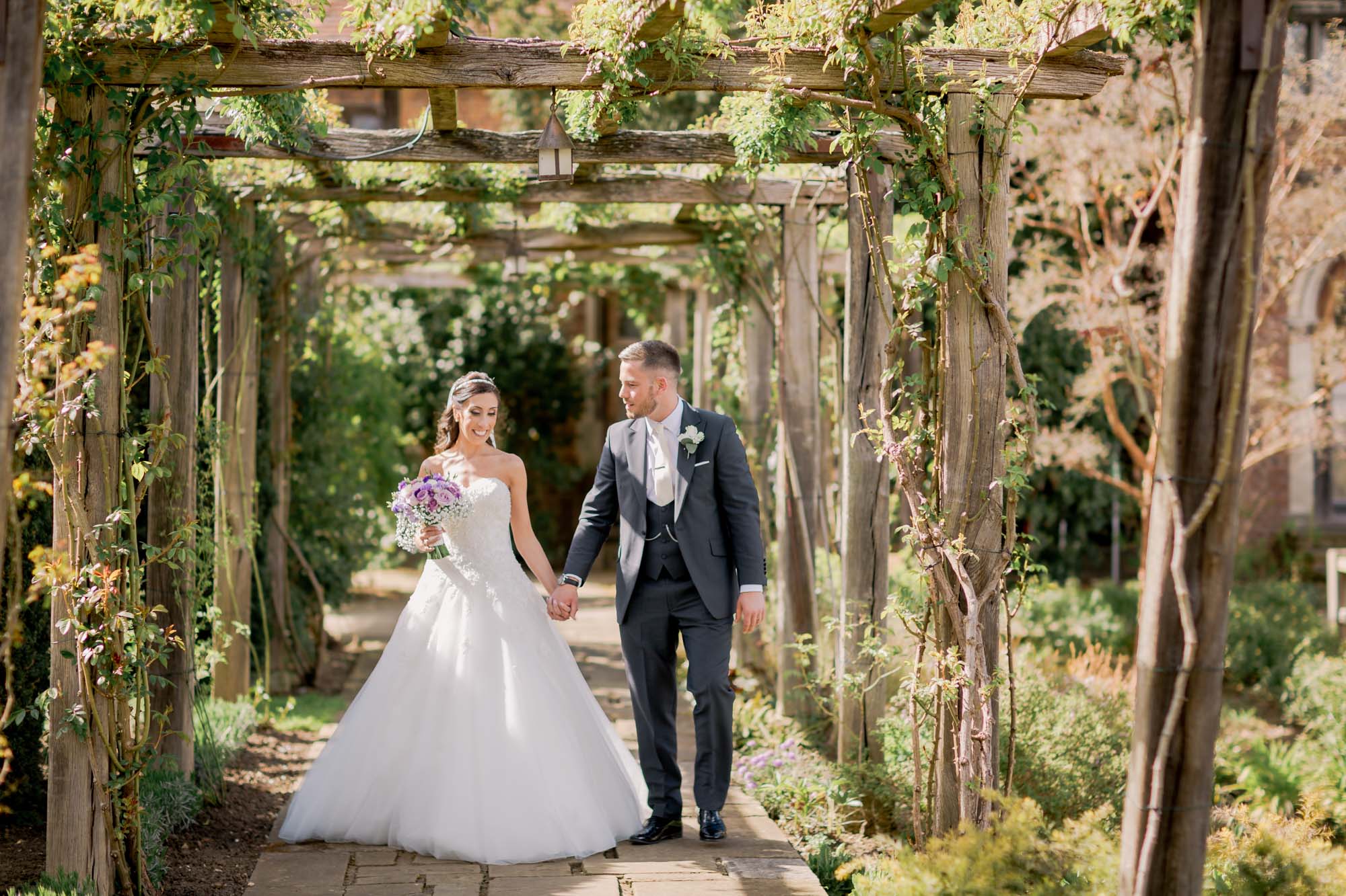 Bride and groom smiling whilst they take a stroll on their wedding day at Great Fosters wedding venue in Egham, Surrey.