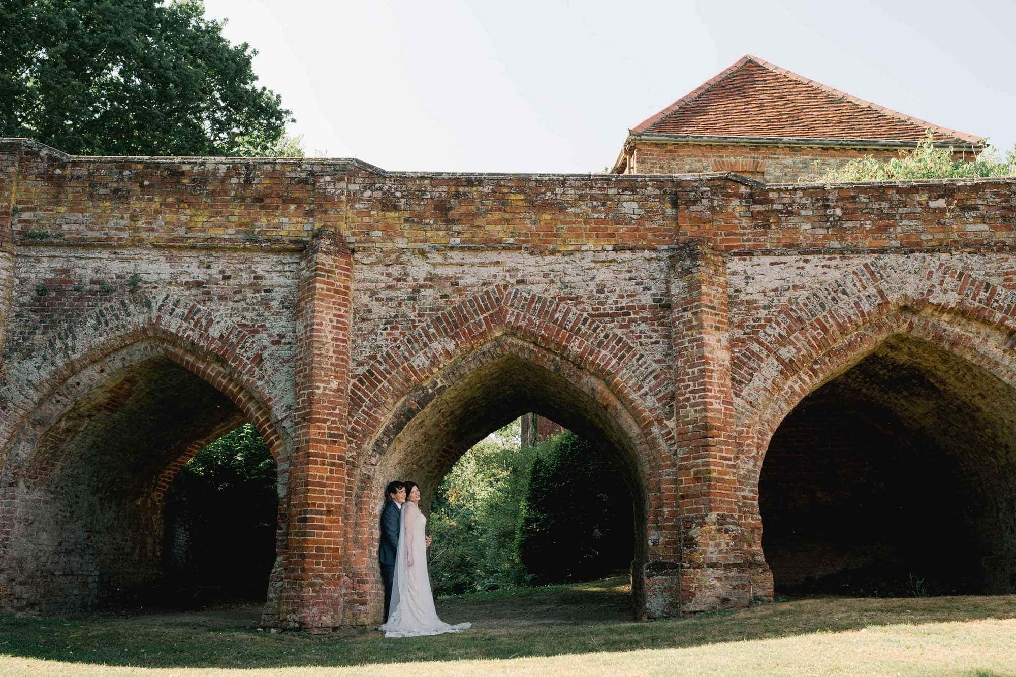 Bride and groom hug closely on their wedding day under the Tudor Bridge at Hedingham Castle in Essex.
