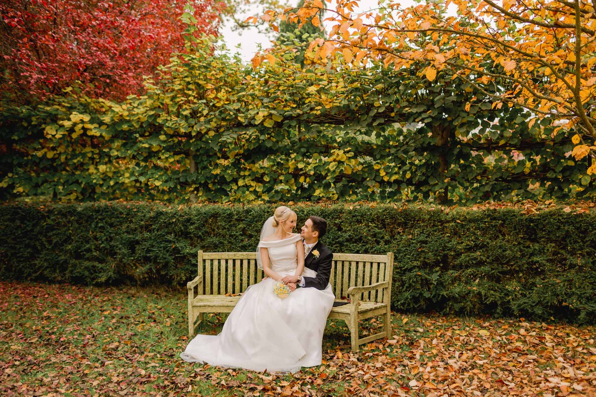 Bride and groom on a bench in the Autumn at Ramster Hall in Chiddingfold.