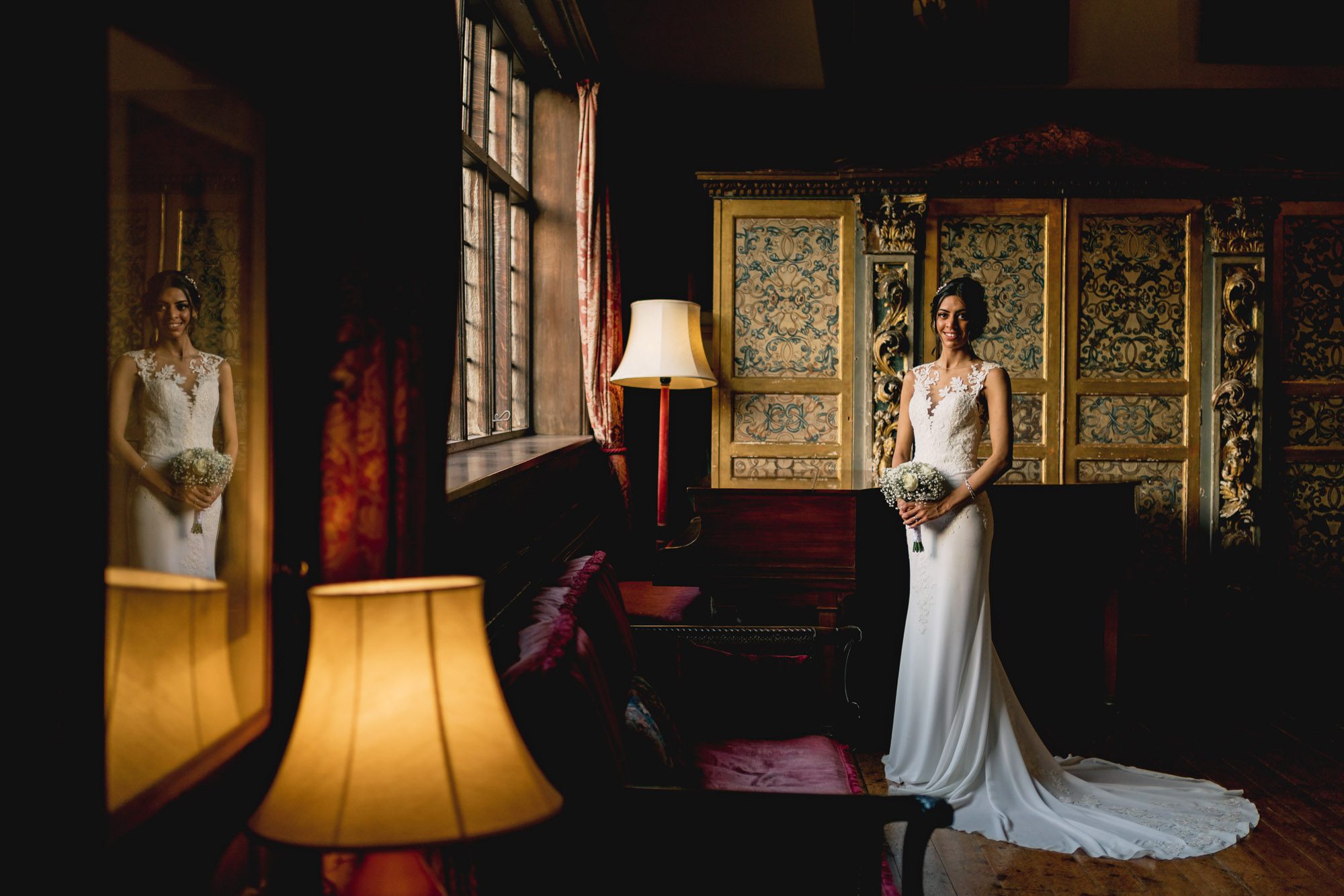A bride in a beautiful wedding dress holding her bouquet of flowers in the Great drawing Room at Ramster hall.