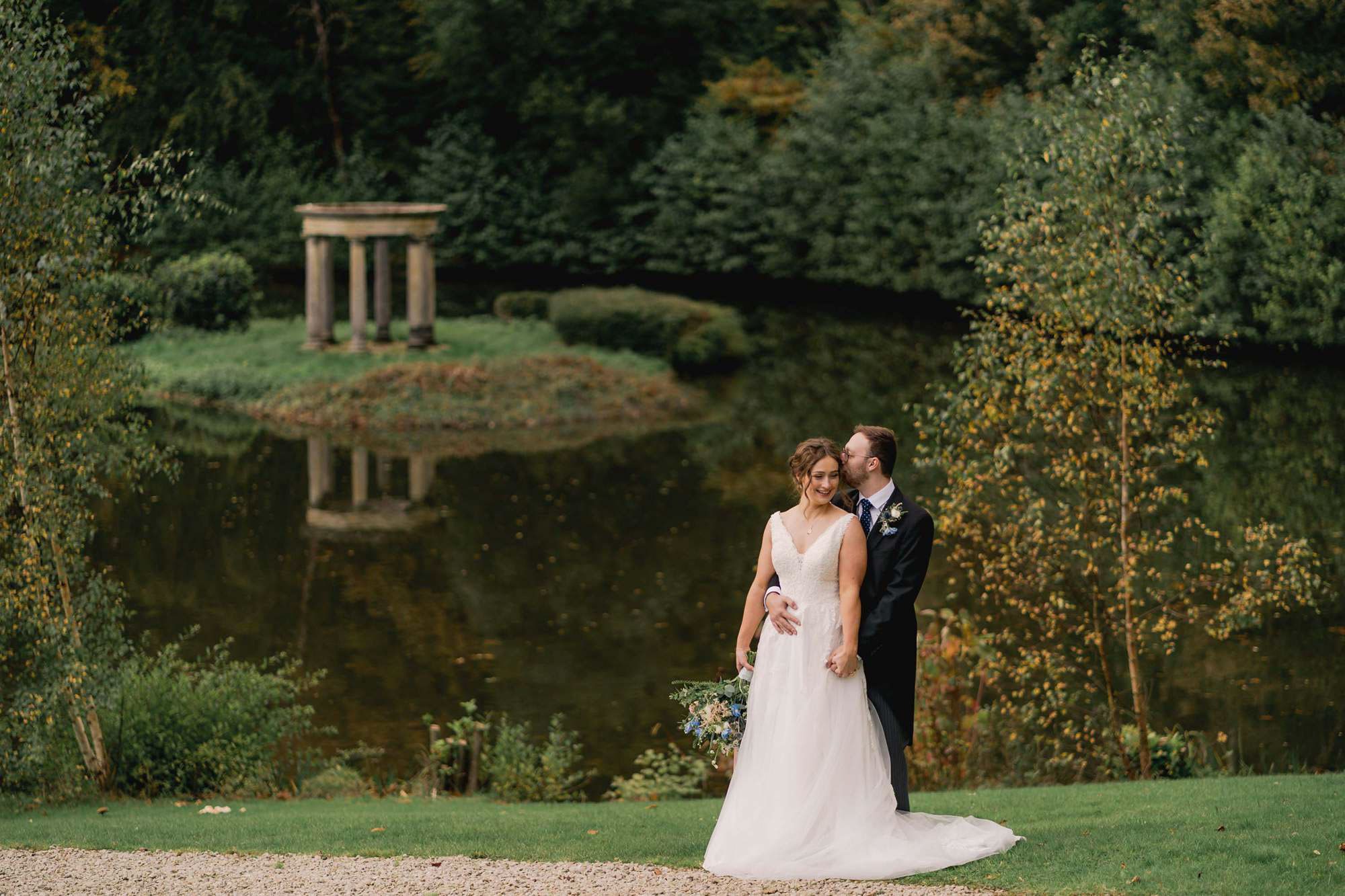 Bride and groom hug closely in front of the lake on their wedding day at Salomons Estate in Tunbridge Wells.