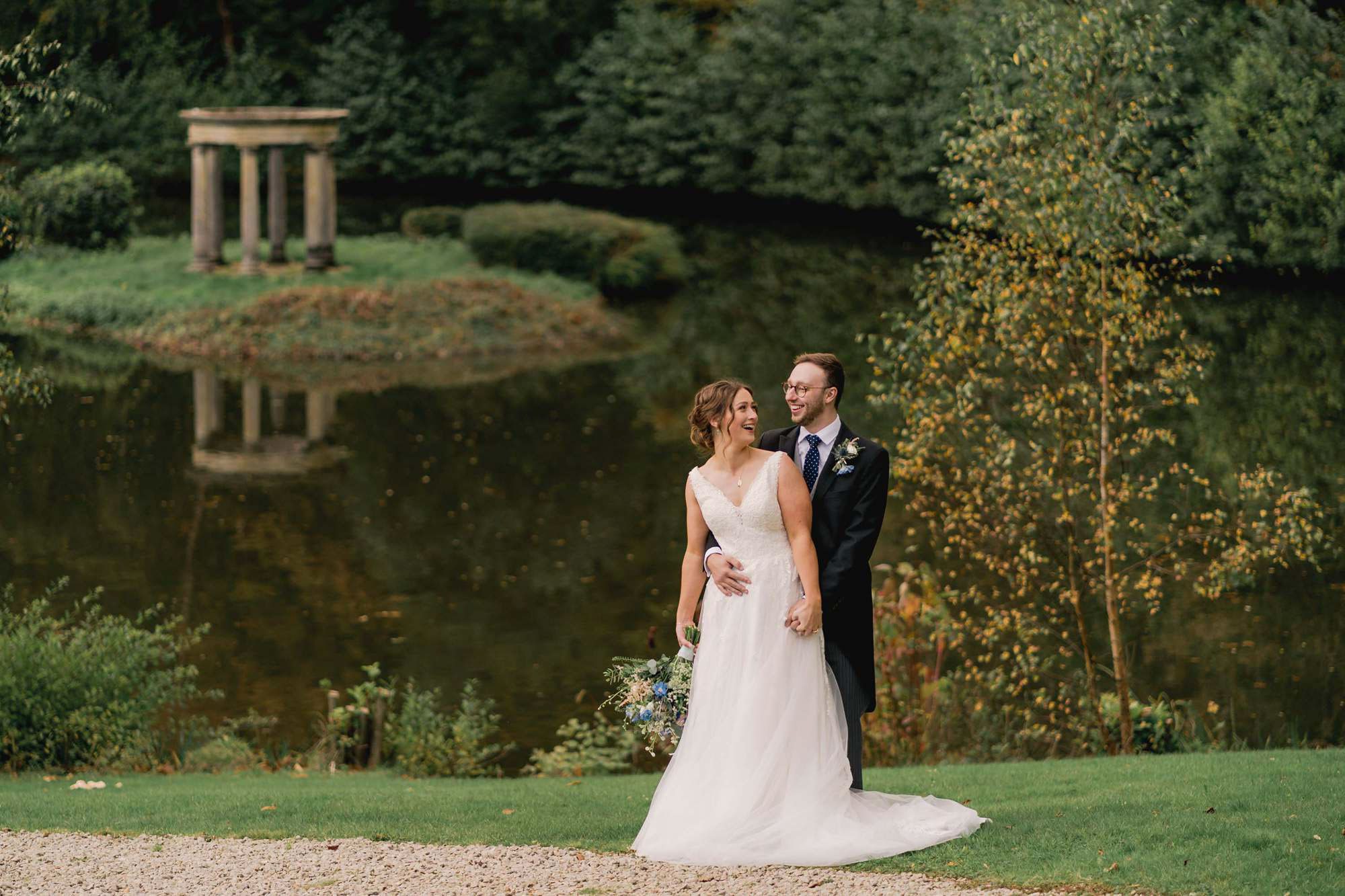 Bride and groom hug closely in front of the lake on their wedding day at Salomons Estate in Tunbridge Wells.