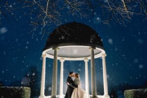 Newly married couple kiss in the snow at Froyle Park.