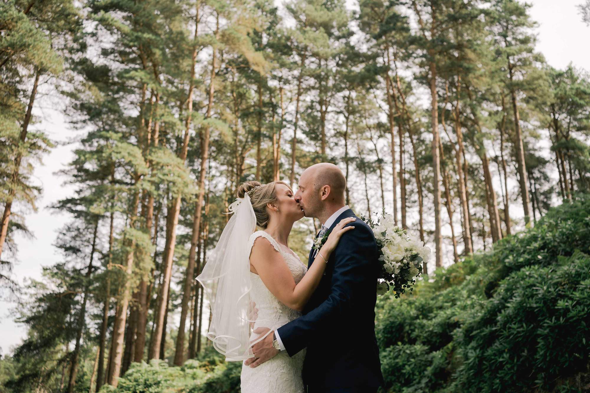 A couple kiss on their wedding day in the woodlands at Old Thorns Hotel in Liphook.