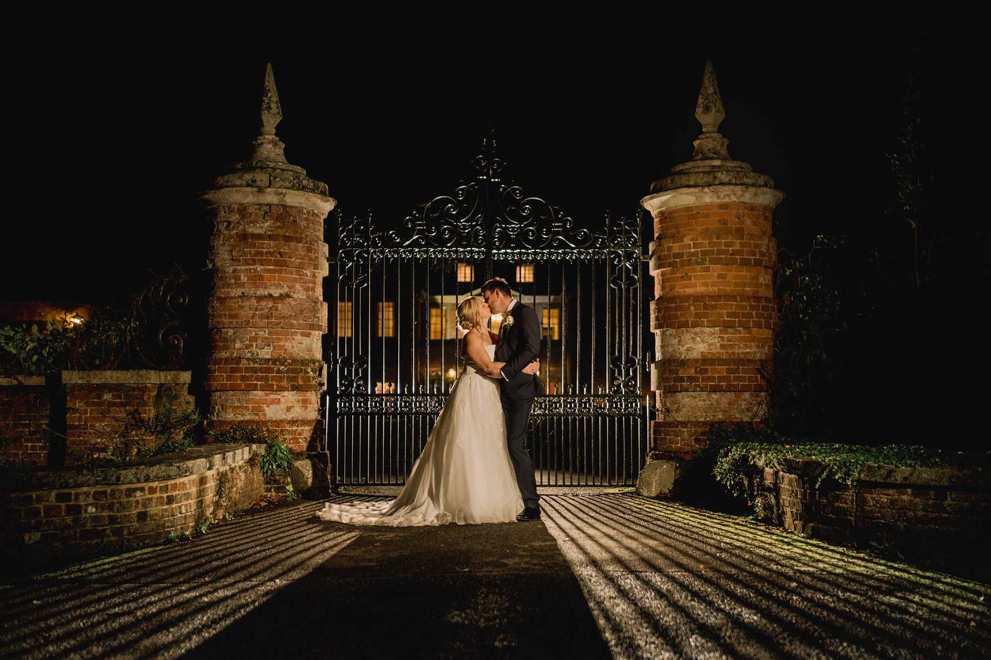Bride and groom kiss in the evening in front of the gates at the entrance of Lainston House.