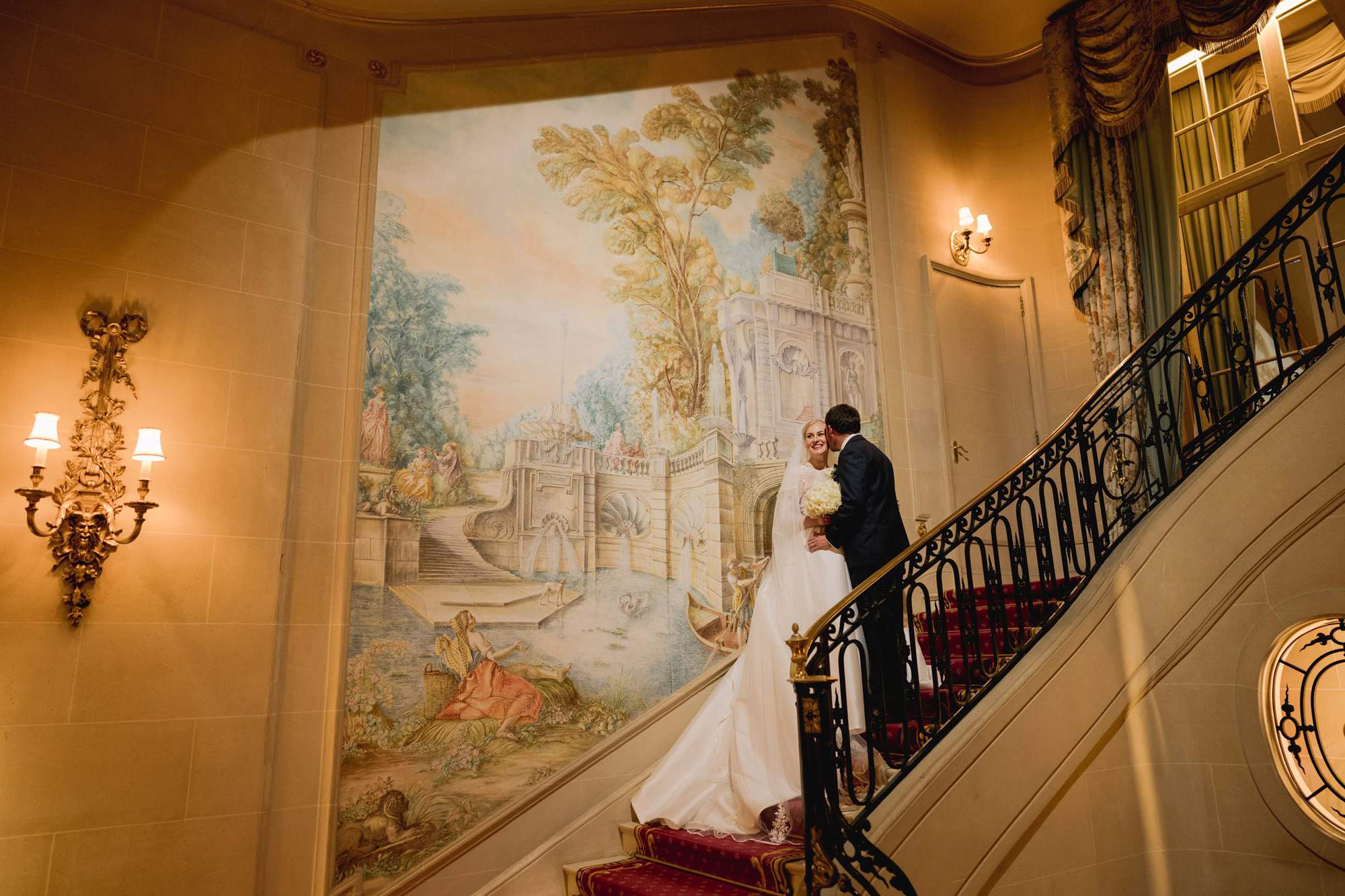 Bride and groom cuddle on the staircase on their wedding day at the Ritz hotel in London.