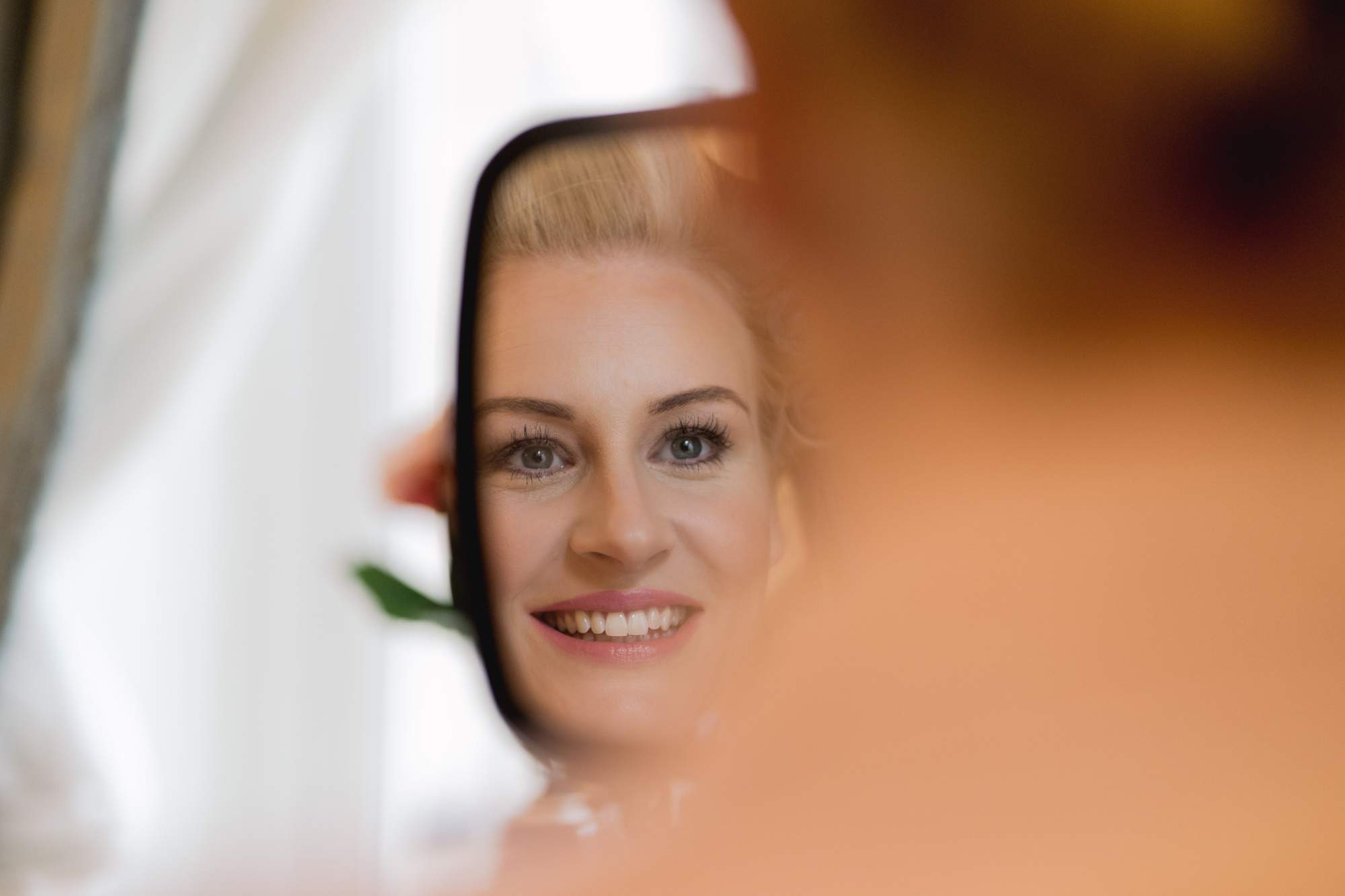 A bride smiling in the mirror on her wedding day at the Ritz hotel in London.