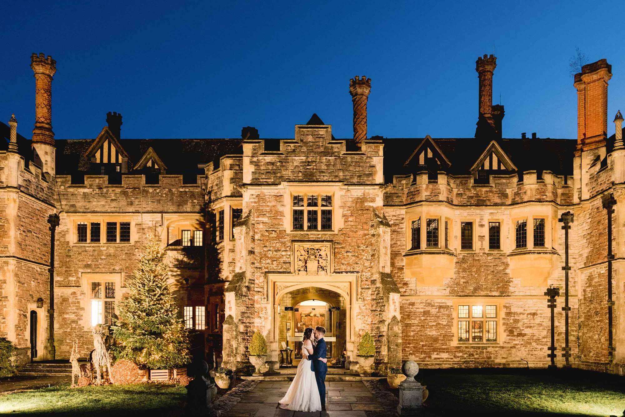 A bride and groom kiss and cuddle under the twilight sky at Rhinefield House in Hampshire.