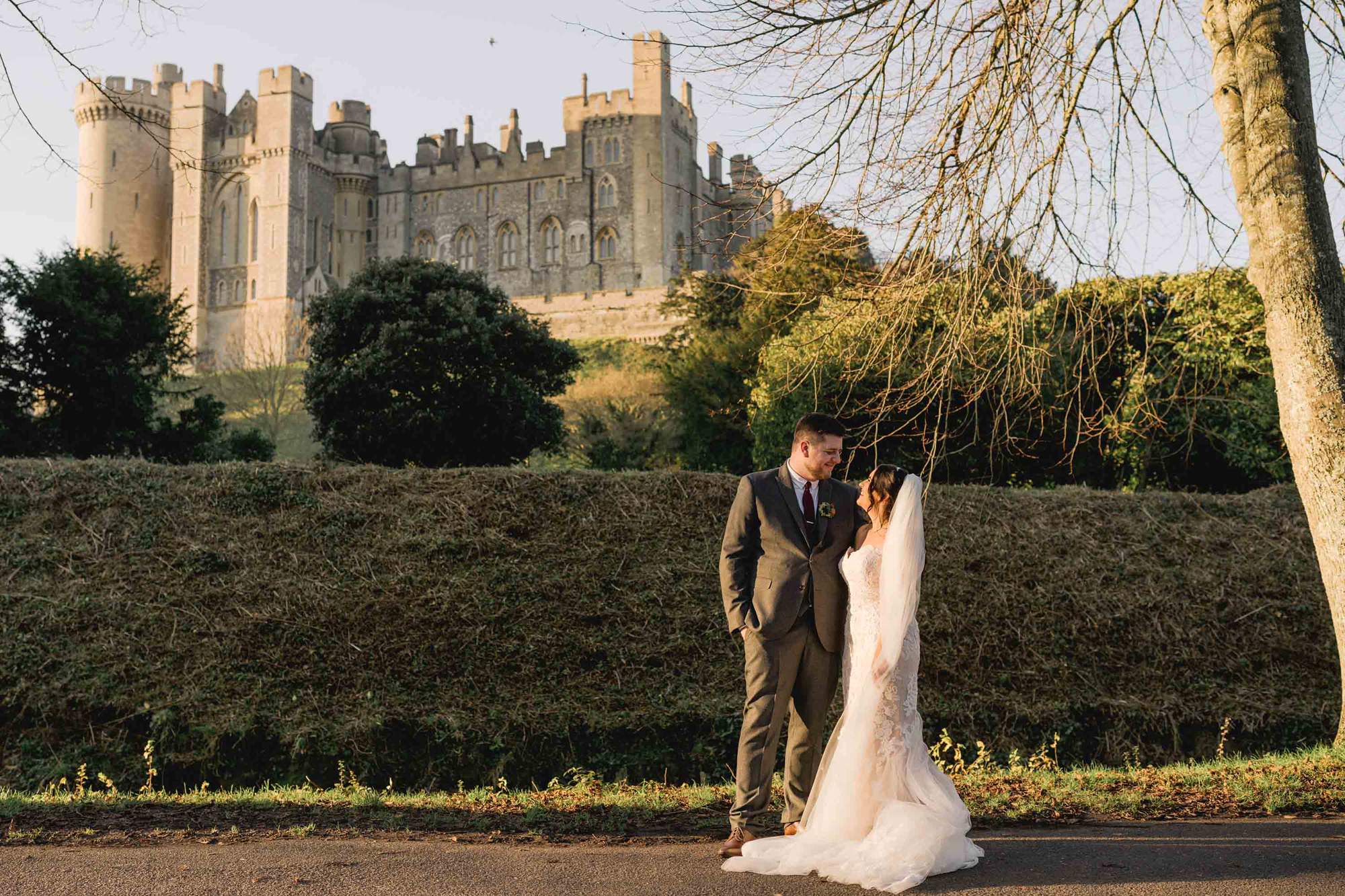 Bride and groom cuddle in front of Arundel Castle on their wedding day.