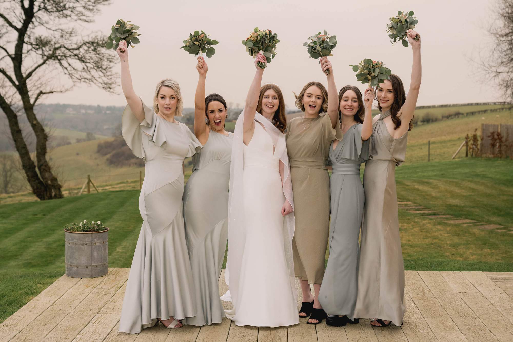bride and her bridesmaids raise their bouquets in celebration at the Barn at Botley Hill wedding venue in the Surrey Hills.