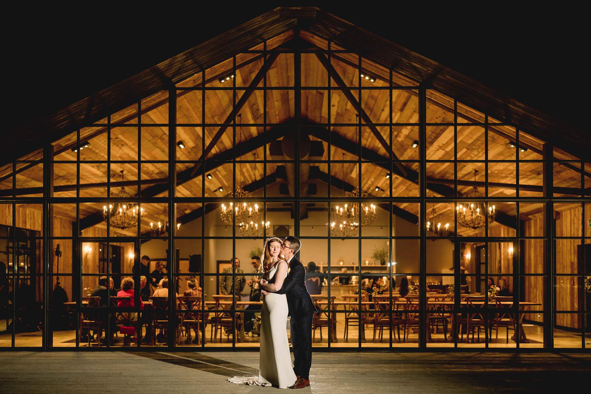 Bride and groom cuddle in front of the Barn at Botley Hill wedding venue in Surrey.