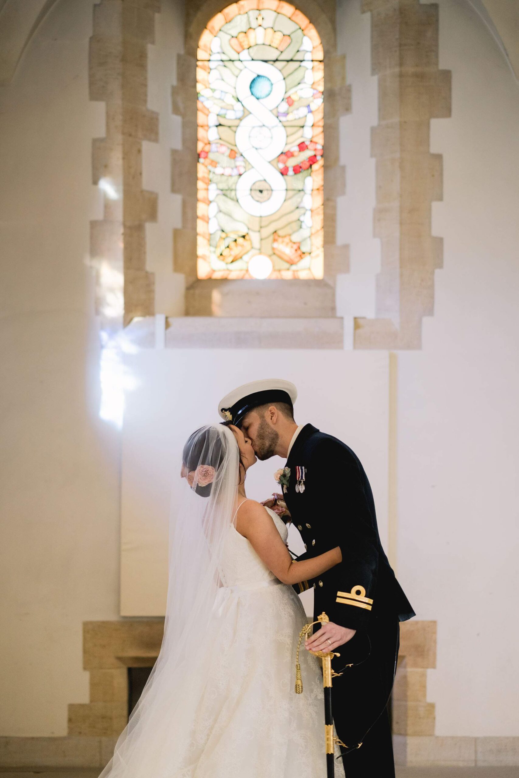 Bride and groom kiss under a stained glass window at the Cathedral in Portsmouth.