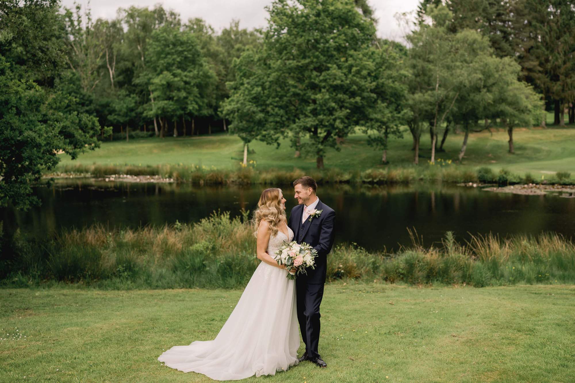 Bride and groom hold each other in front of the lake at Cottesmore Golf Club.