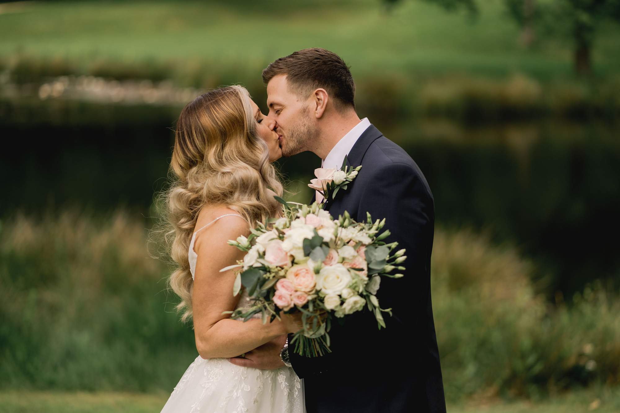 Bride and groom kiss each other in front of the lake at Cottesmore Golf Club.