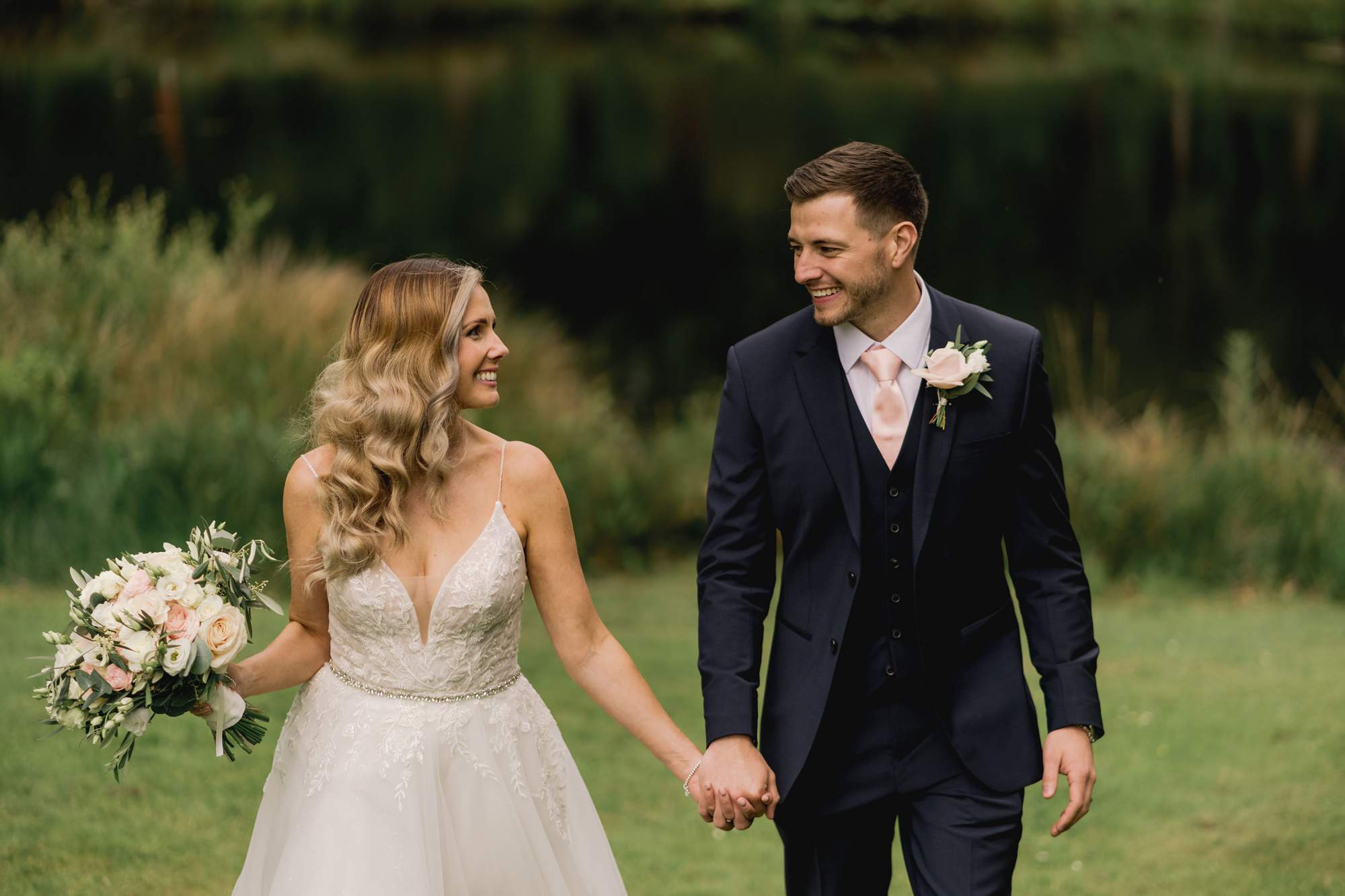 Bride and groom hold hands and take a stroll in front of the lake at Cottesmore Golf Club.