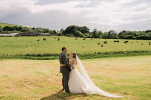 Newlyweds cuddle in a nearby field on their wedding day at Tottington Manor in Sussex.