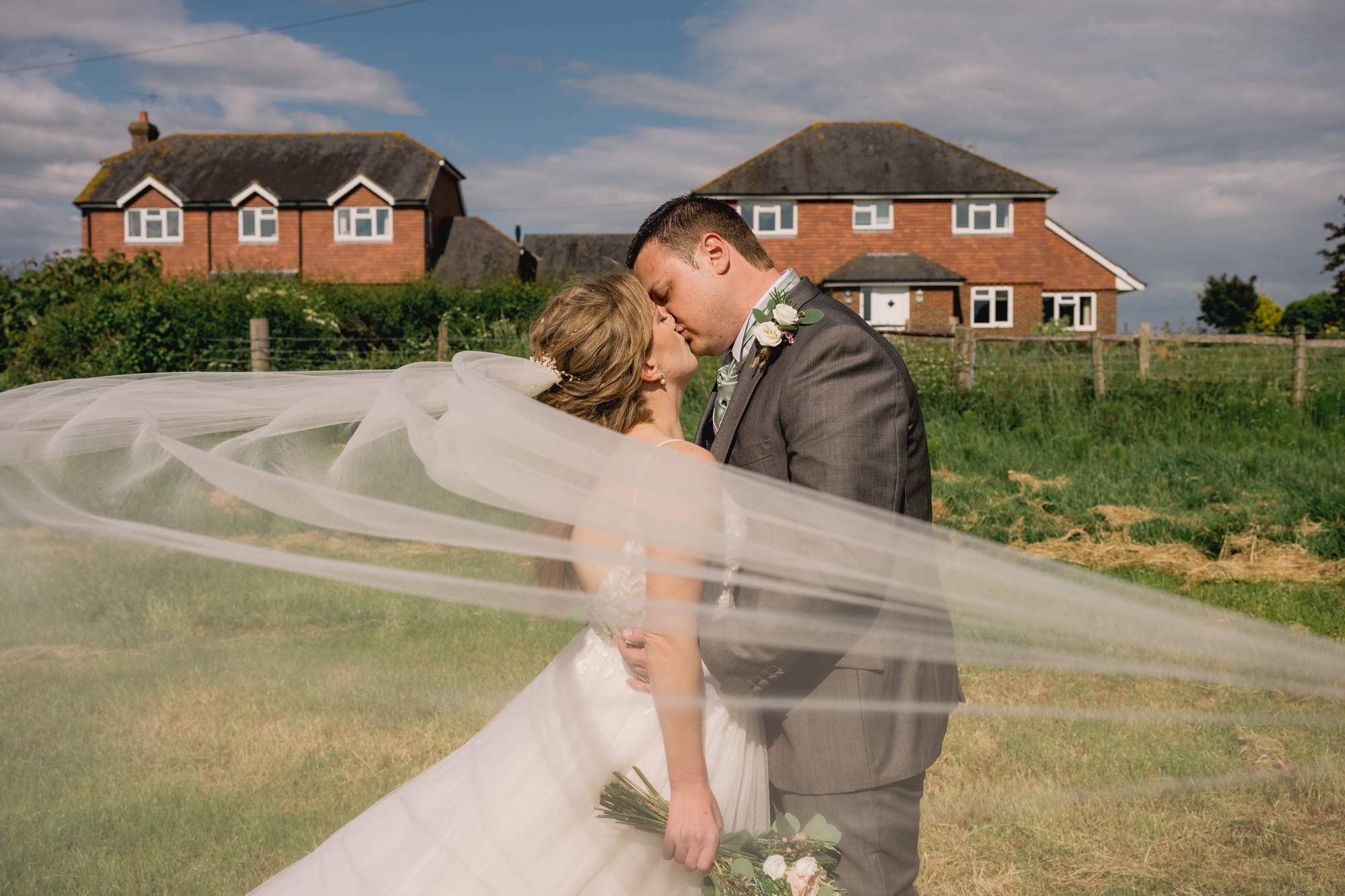 The bride's wedding veil blows in the wind at Tottington Manor in the Sussex countryside.