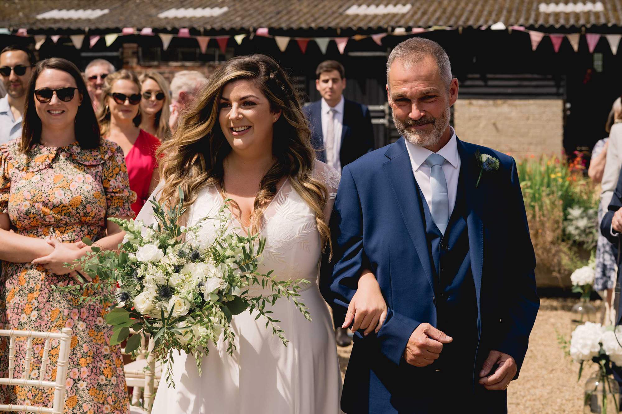 The bride and her father walk down the aisle at a wedding at the Sussex Barn wedding venue in Hellingly.