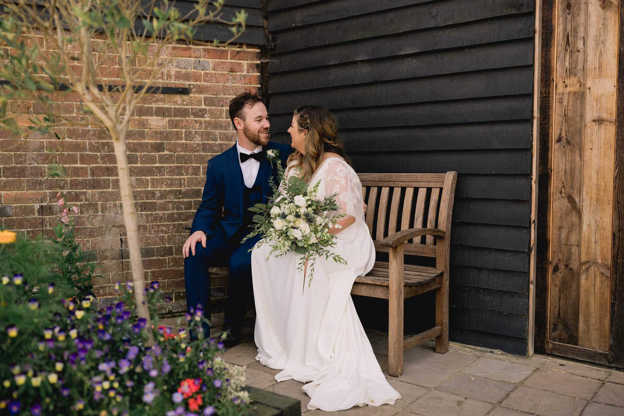Bride and groom cuddle on a bench outside the Sussex Barn in Hellingly.