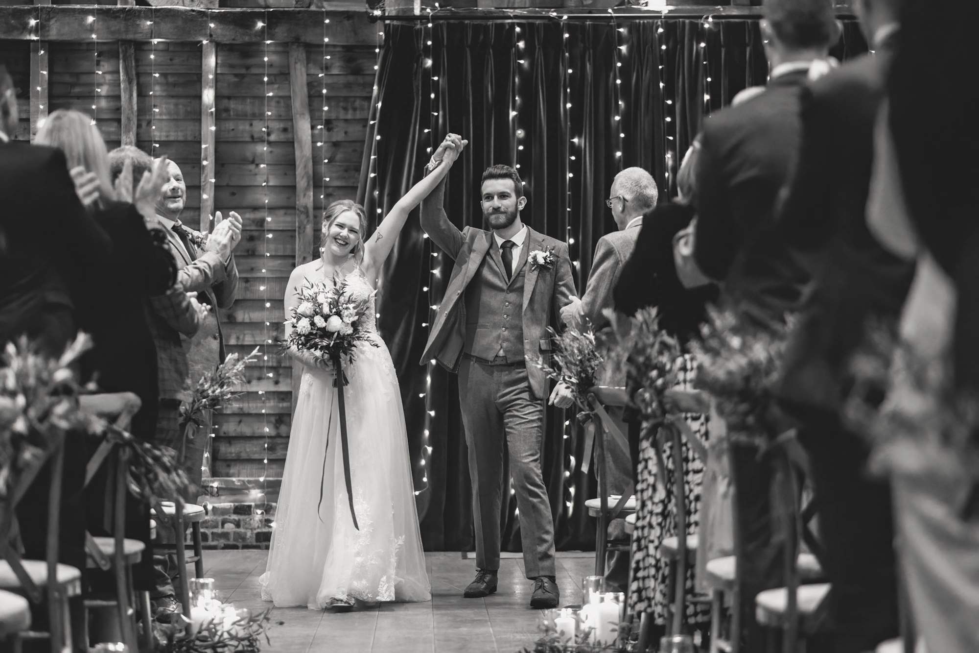 Bride and groom give a cheer and hold their hands in the air after the wedding ceremony in the barn at The Farmhouse at Redcoats.