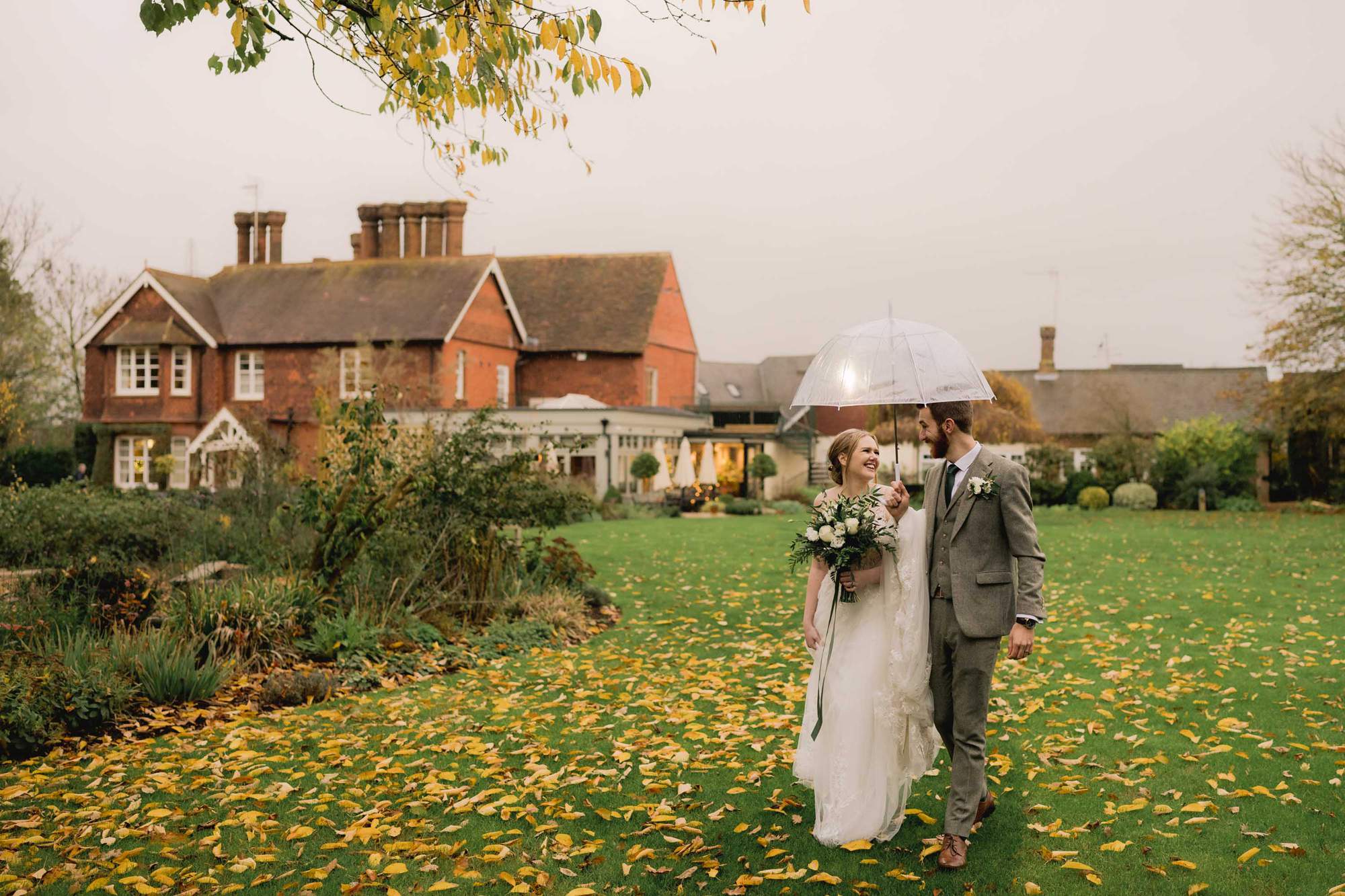 Bride and groom take a stroll under a clear umbrella at The Farmhouse at Redcoats in Hitchin.