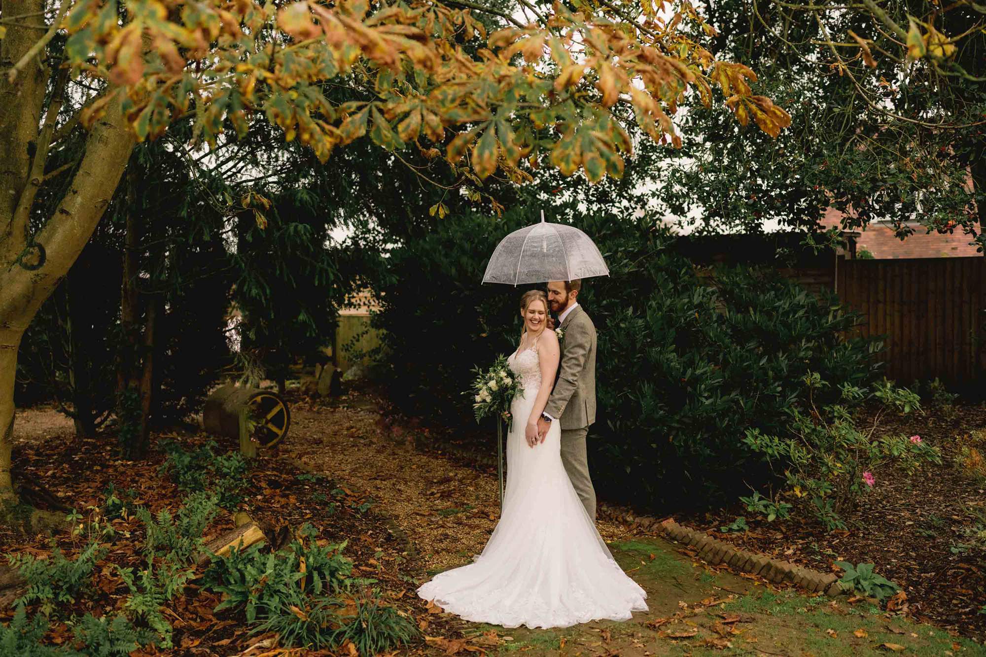 Bride and groom have a cuddle under an umbrella at The Farmhouse at Redcoats in Hitchin.