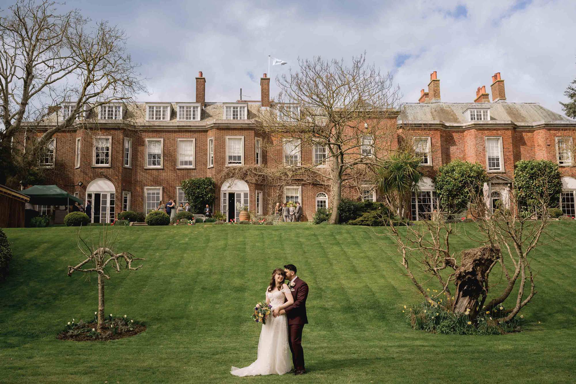 Bride and groom hug closely on their wedding day with Pelham House as the backdrop.