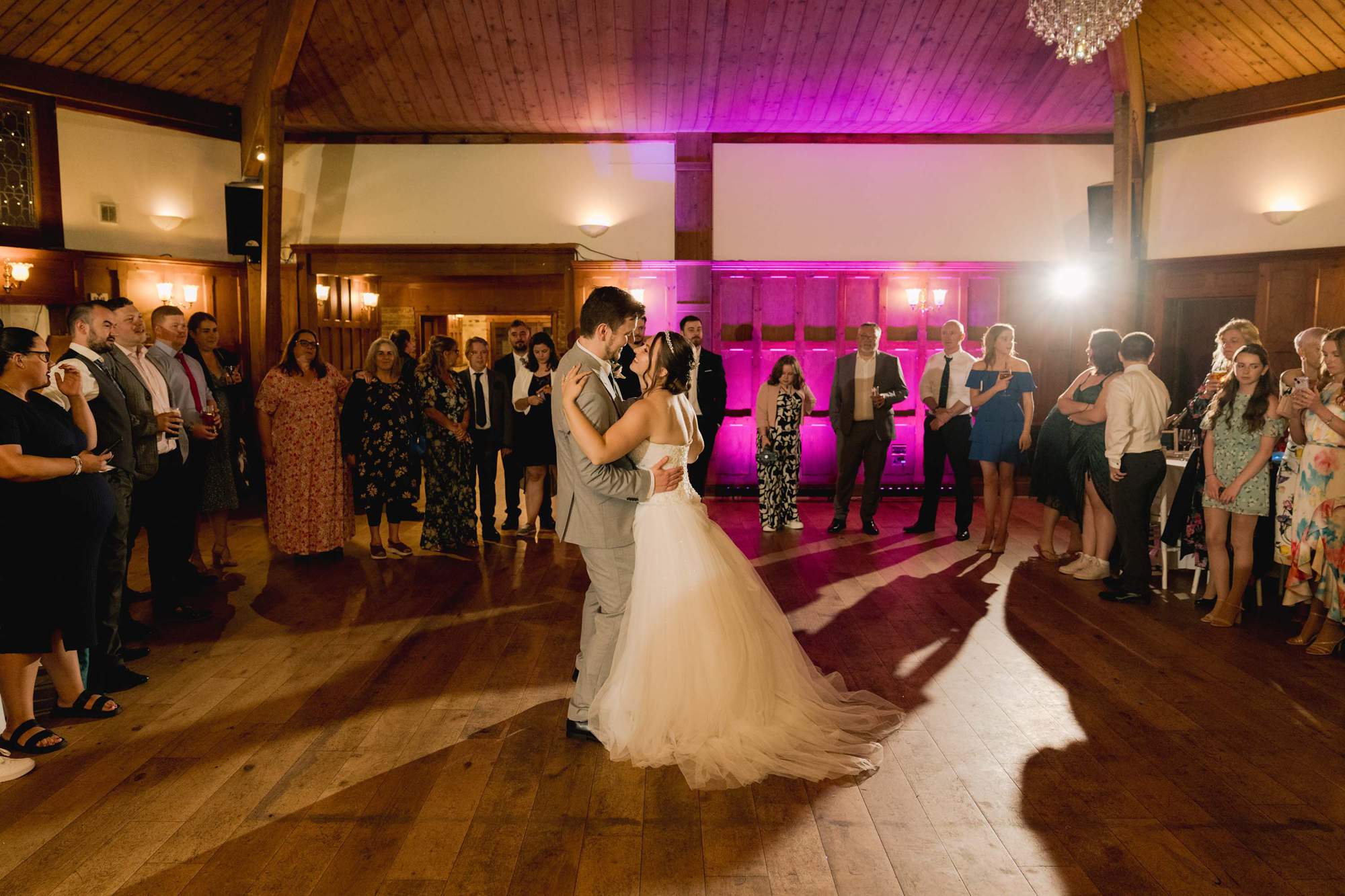 Bride and groom have a first dance in pink lighting at the Ravenswood Hotel in Sussex.