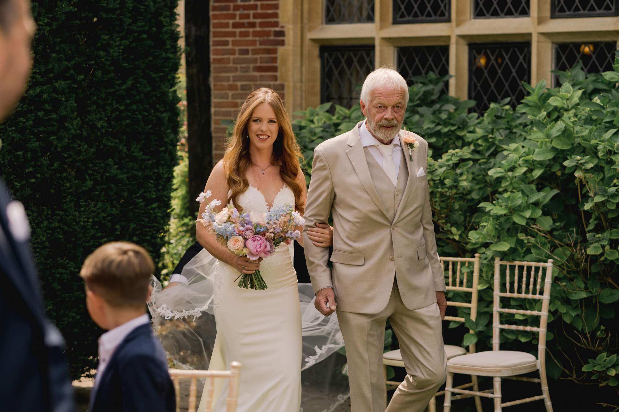 A bride walks down the aisle with her father during an outdoor ceremony at Amberley Castle in West Sussex.