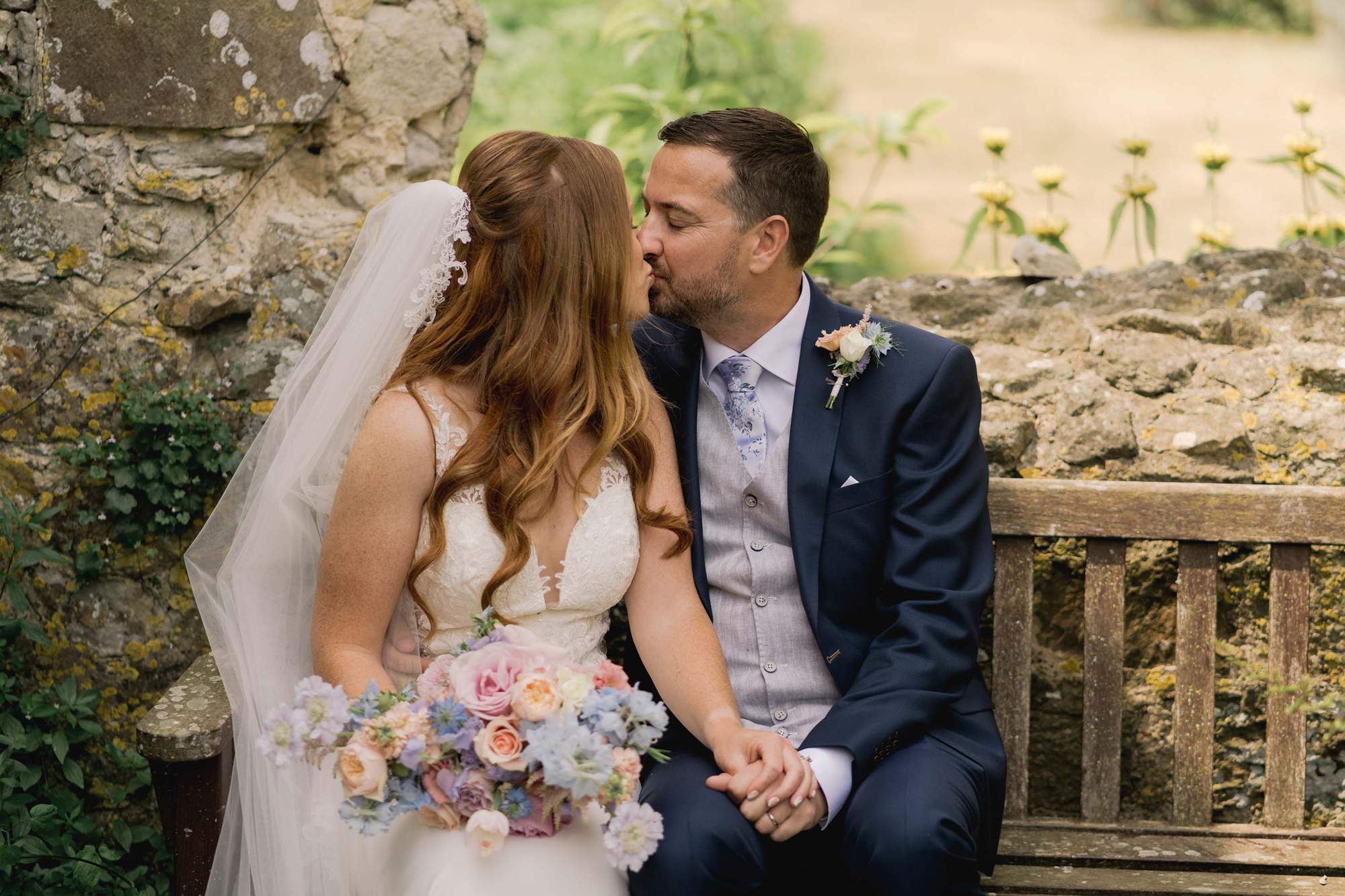 Bride and groom kiss on their wedding day on a bench at Amberley Castle.
