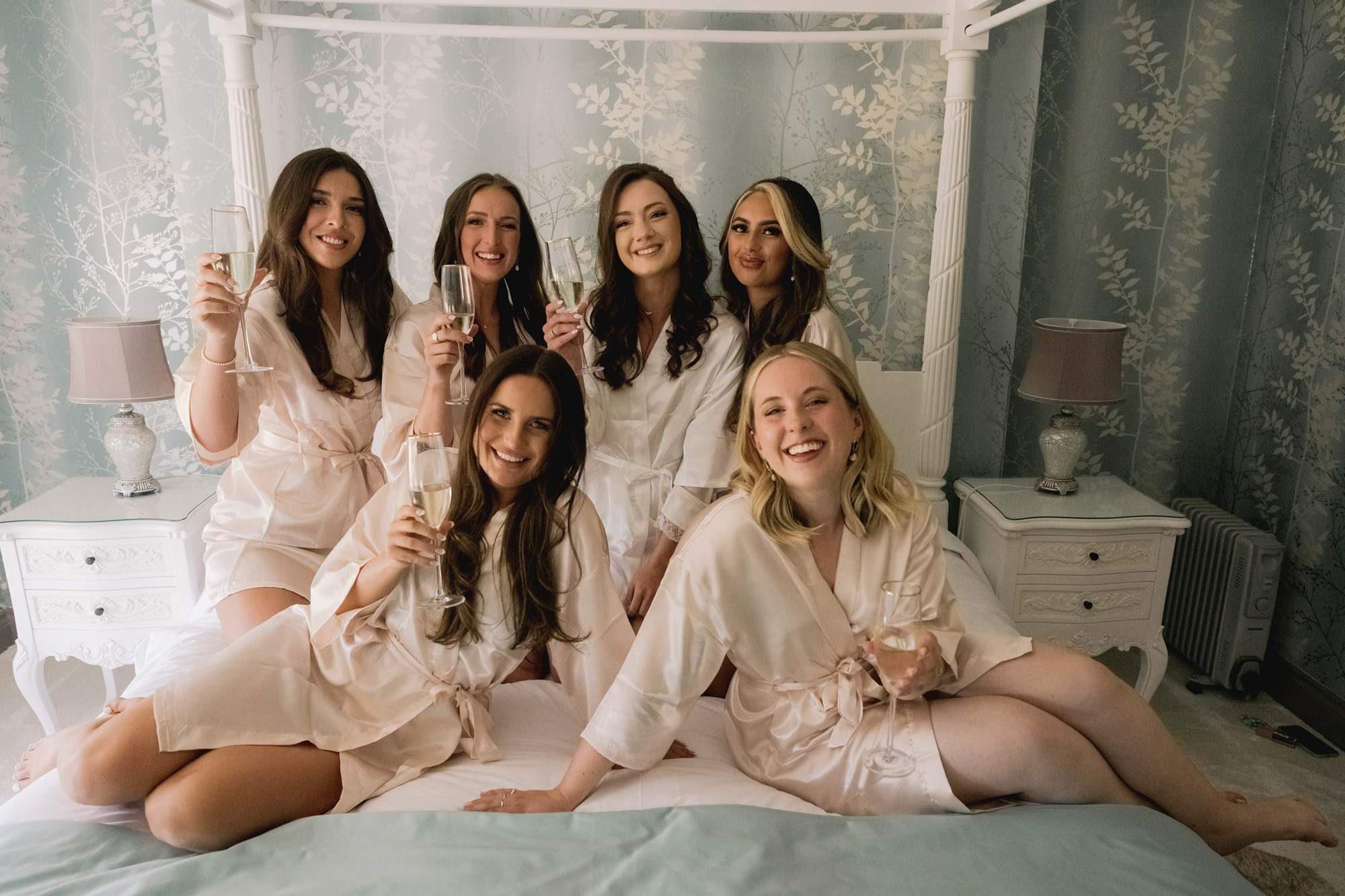 Bride and her bridal party celebrate with champagne on the four poster bed at Southdowns Manor.