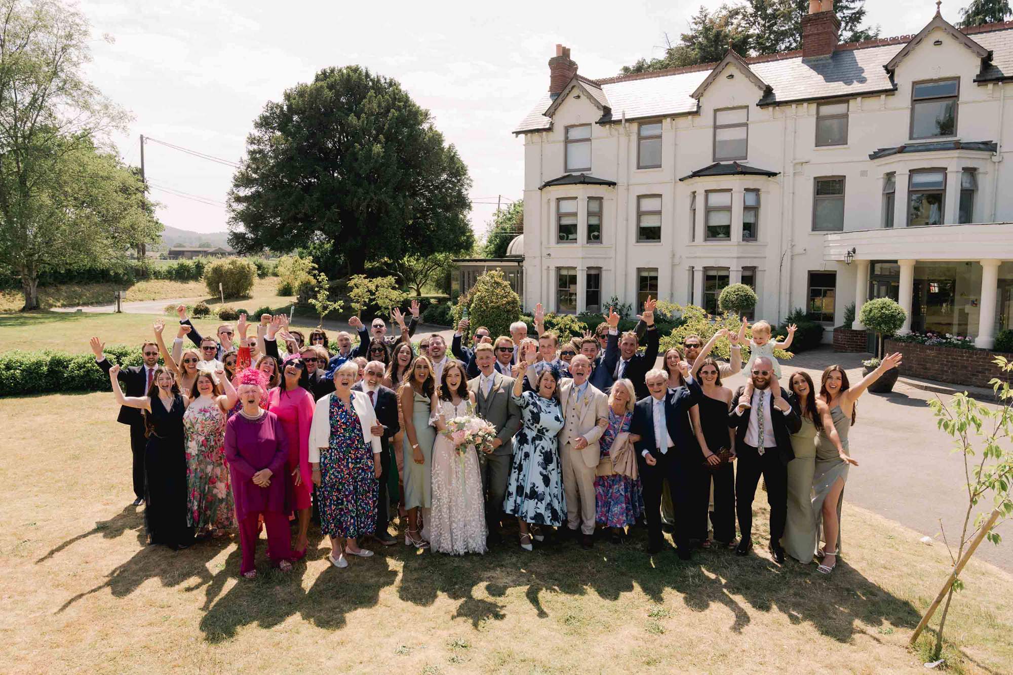 Bride and groom cheer with all their wedding guests with Southdowns Manor in the corner of the picture.