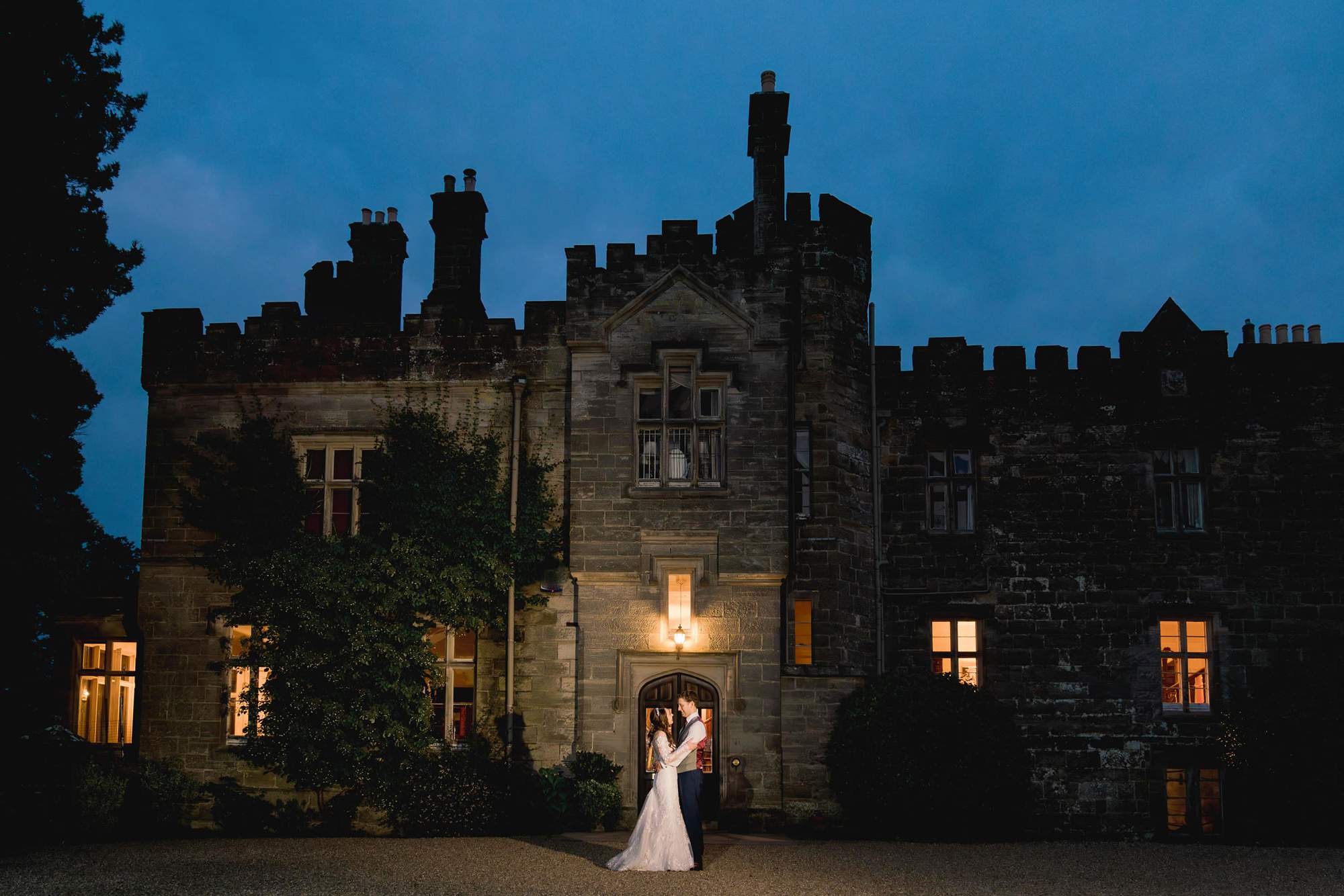 Bride and groom cuddle at twilight in front of Wadhurst castle in Sussex.