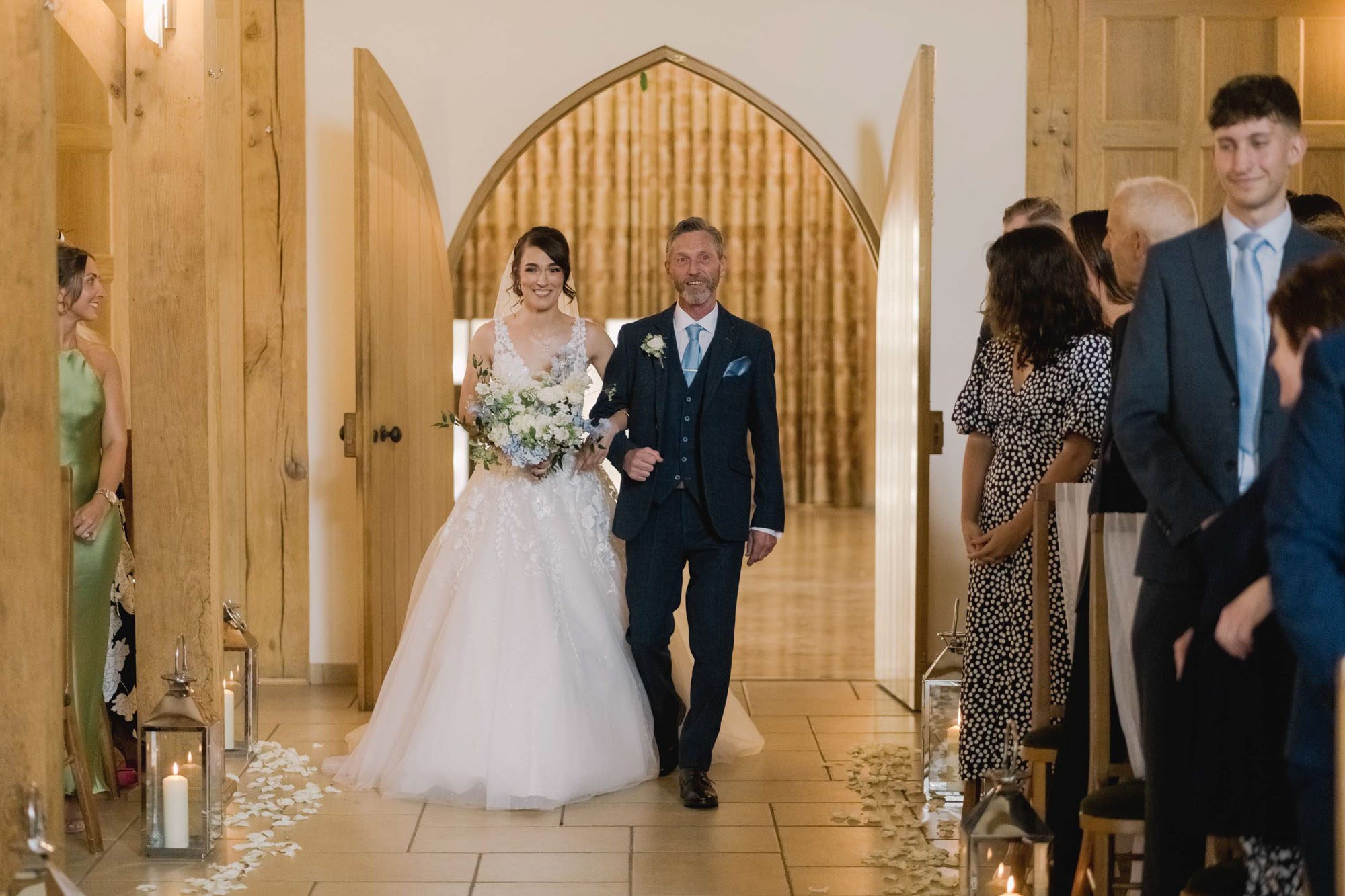 A bride walks down the asile with her father on her wedding day at Rivervale Barn in Hampshire.