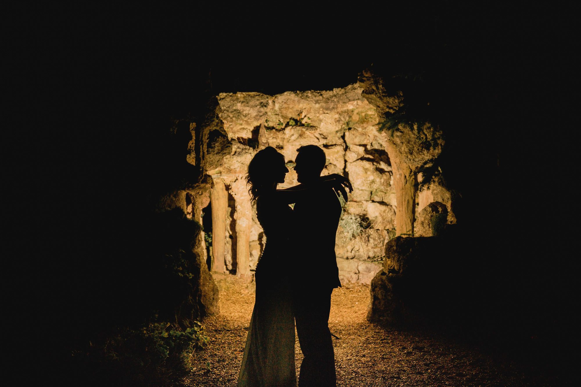 Bride and groom silhoutted in front of the cave in the gardens at Wotton House.